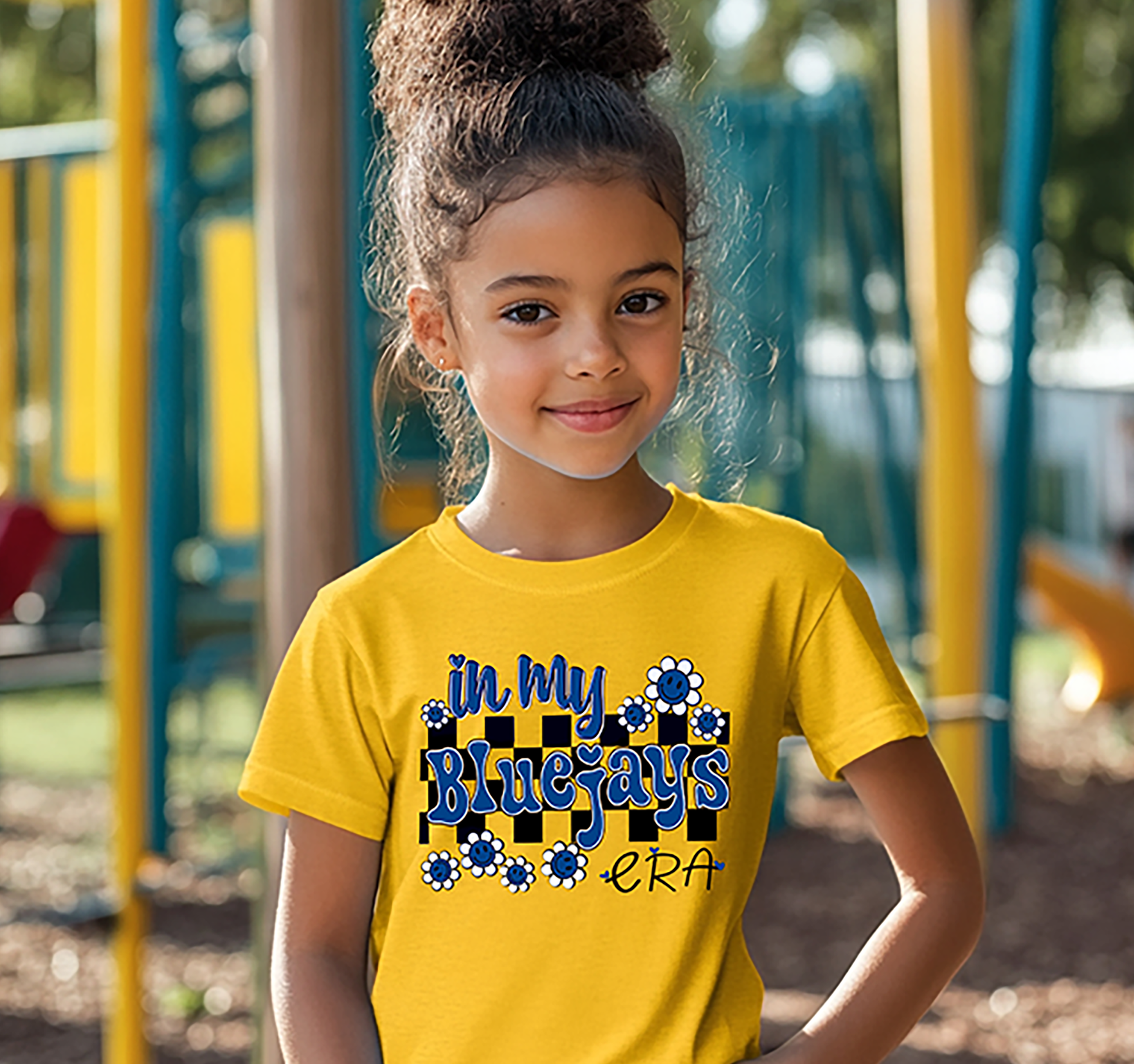 Child wearing a yellow t-shirt with 'In My Bluejays Era' design on a playground.